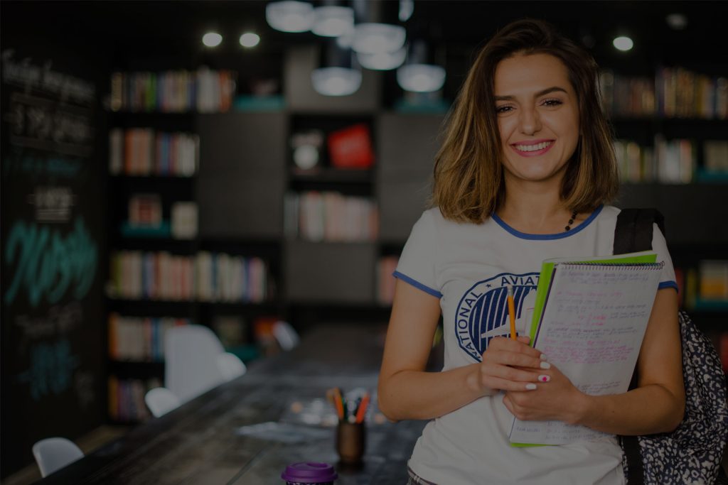 Smiling learner holding notebooks in a library